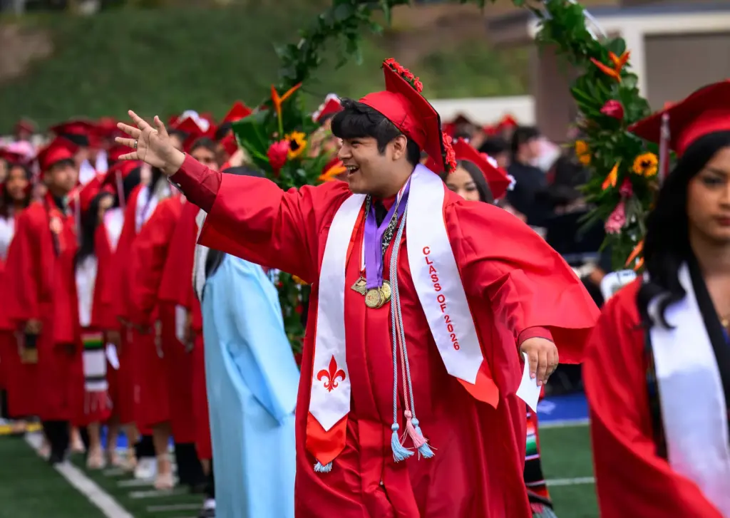 An excited graduate waves to his family as he walks...
