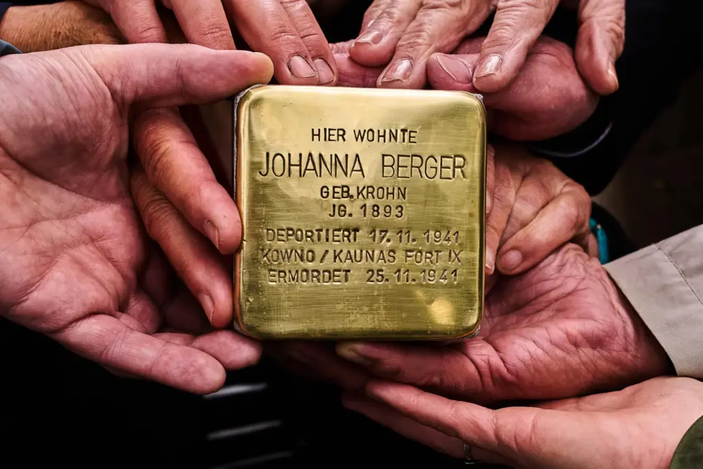 Relatives shows a photo a palm-sized brass Holocaust plaque