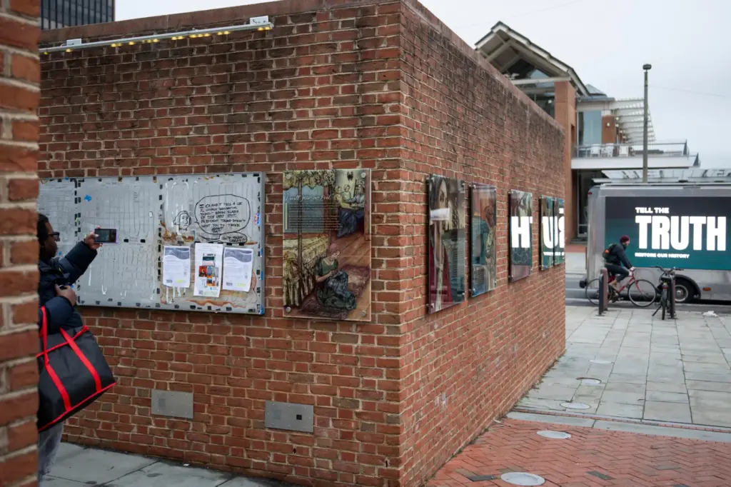 An attendee photographs a still-missing section of signs as people gather for a rally celebrating the reinstallation of a slavery exhibit