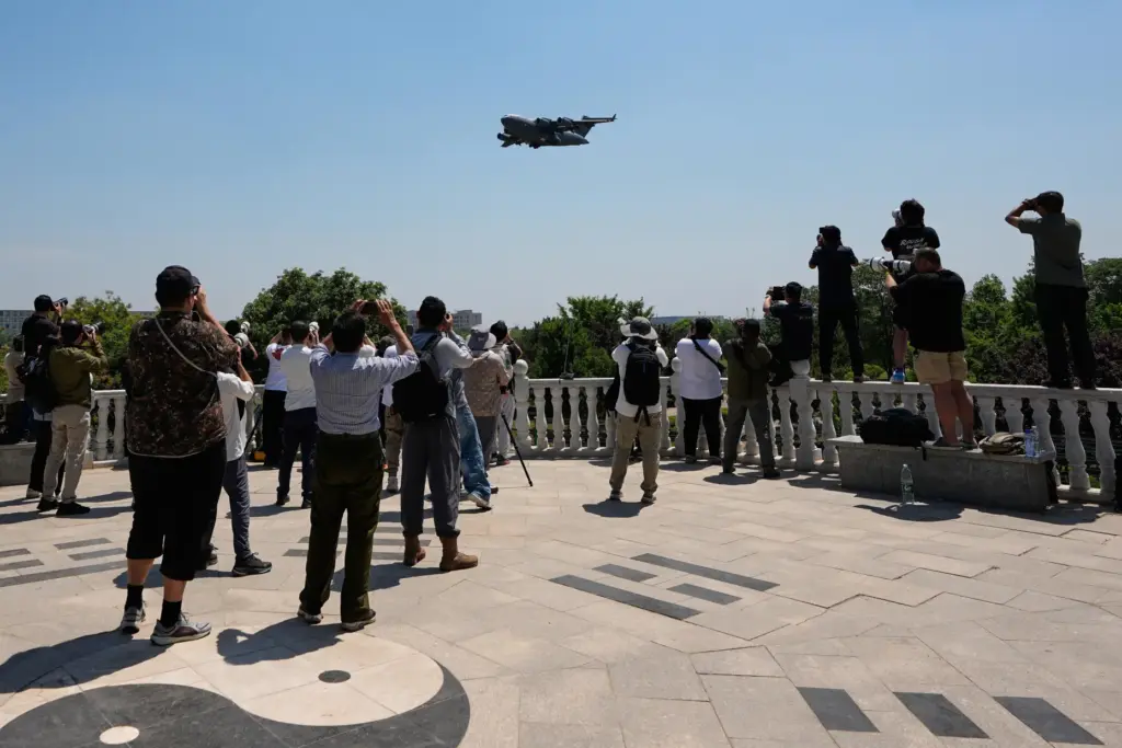 People gather at a viewing platform of a public park film a U.S. Air Force Boeing C-17 Globemaster III transport aircraft