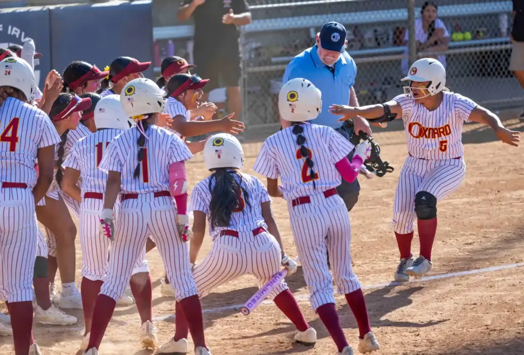 Oxnard third baseman Rachel Godoy signals to her excited teammates...