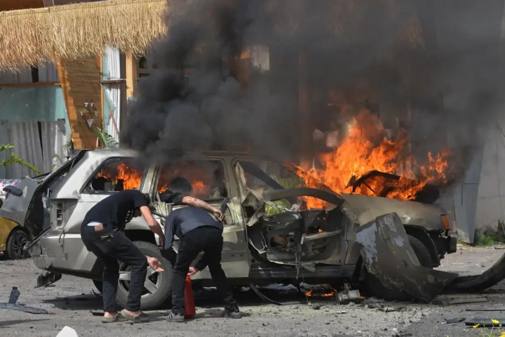 A person is seen inside a burning vehicle as men attempt to put out the fire.
