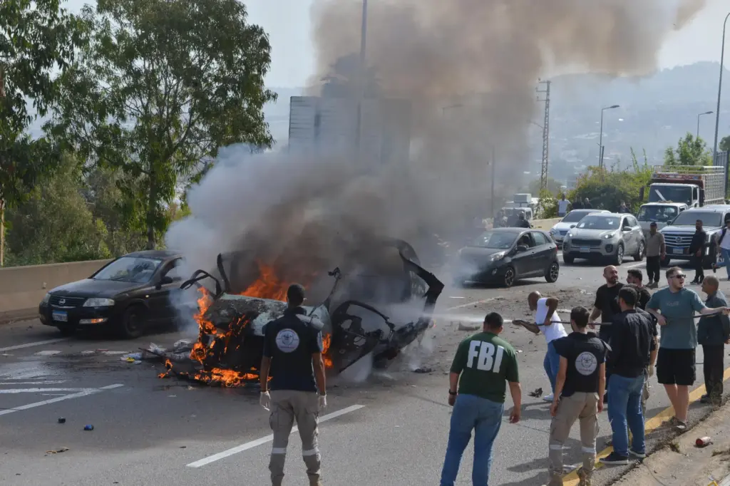Security forces and emergency responders gather around a burning vehicle...