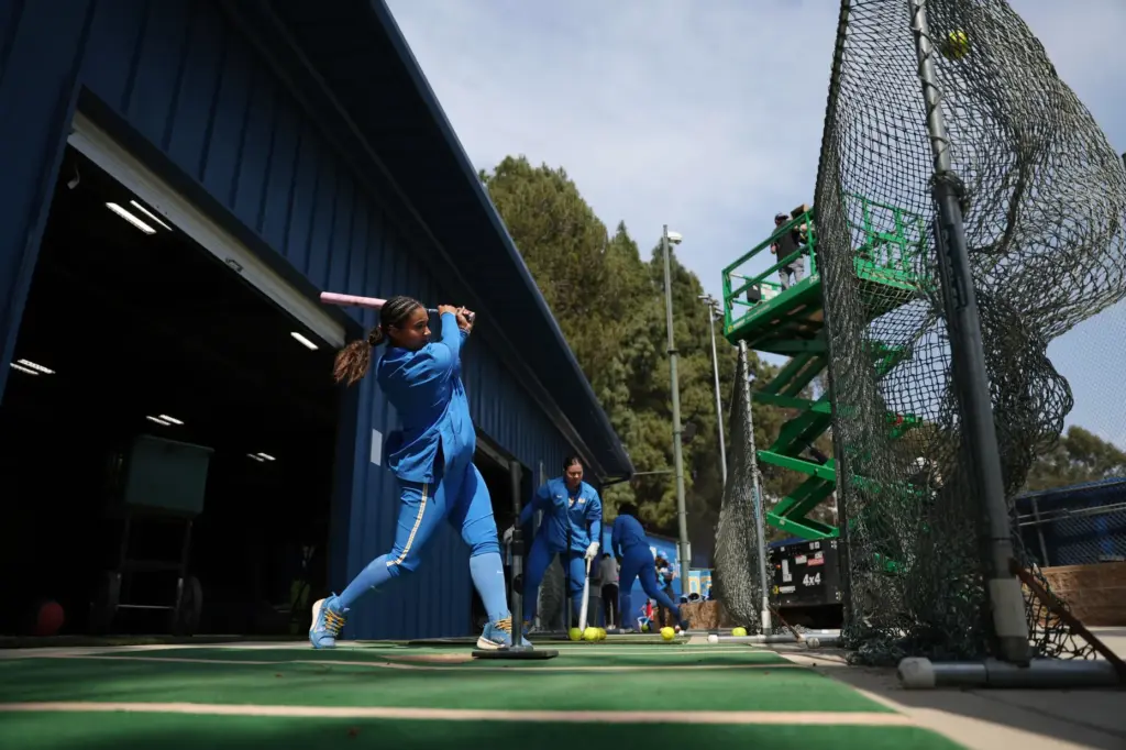UCLAâs Jordan Woolery, left, takes practice swings off a tee...