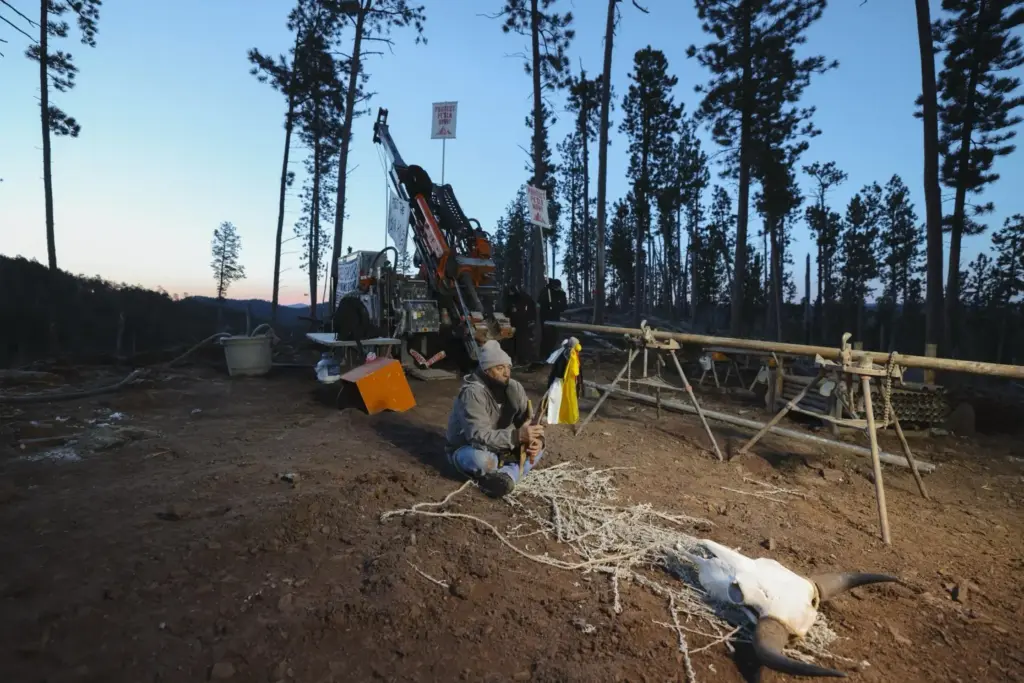 A demonstrator sits cross legged in front of drilling equipment...