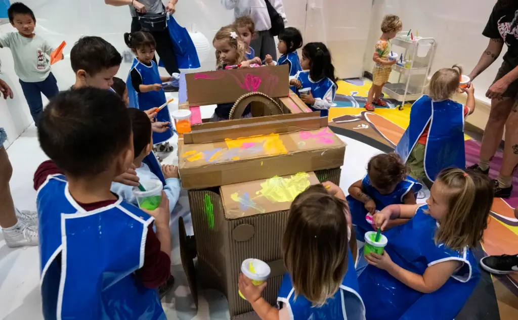 Kids paint a cardboard car and the walls during opening...
