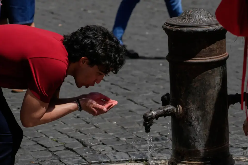 A man drinks water at a fountain in downtown Rome.