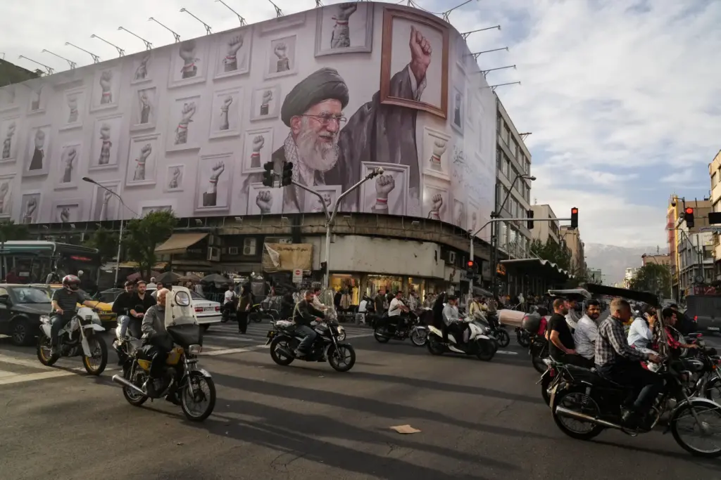 Motorbikes drive past a billboard showing the late Iranian Supreme Leader Ayatollah Ali Khamenei.