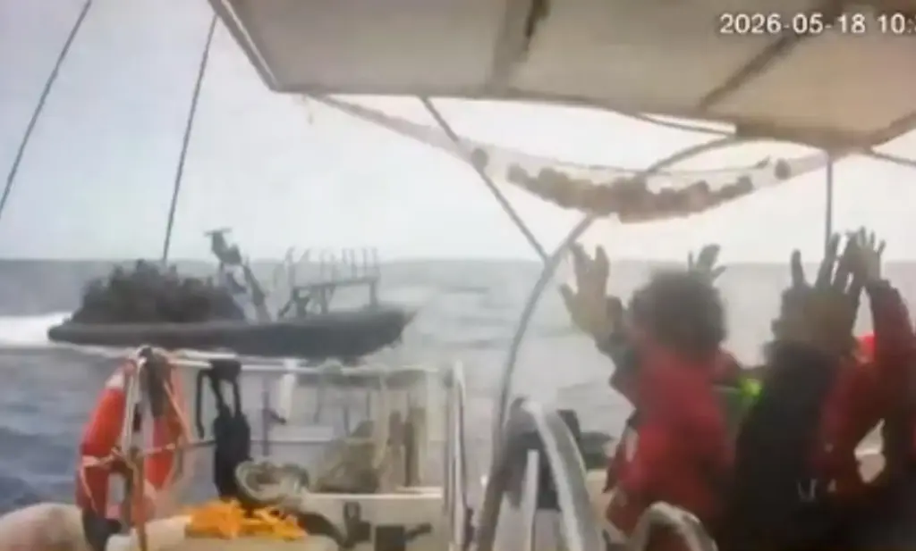 Activists aboard a flotilla boat with their hands in the air as a boat approaches.