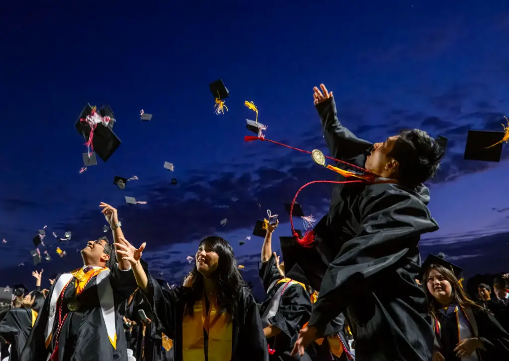 Graduates toss their caps into the air following the Troy...