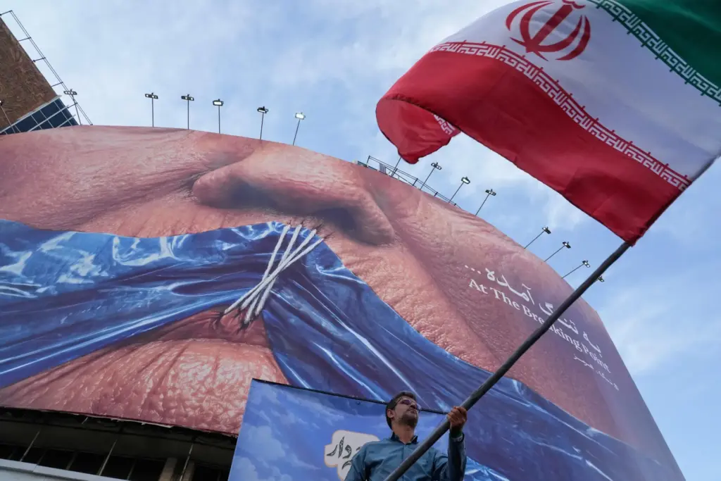 A man waves an Iranian flag under a billboard with President Donald Trump's lips sewn together.