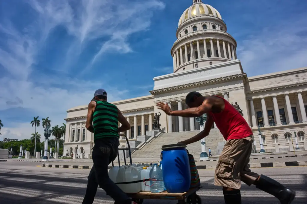 People carry containers of water past the Capitol in Havana,...