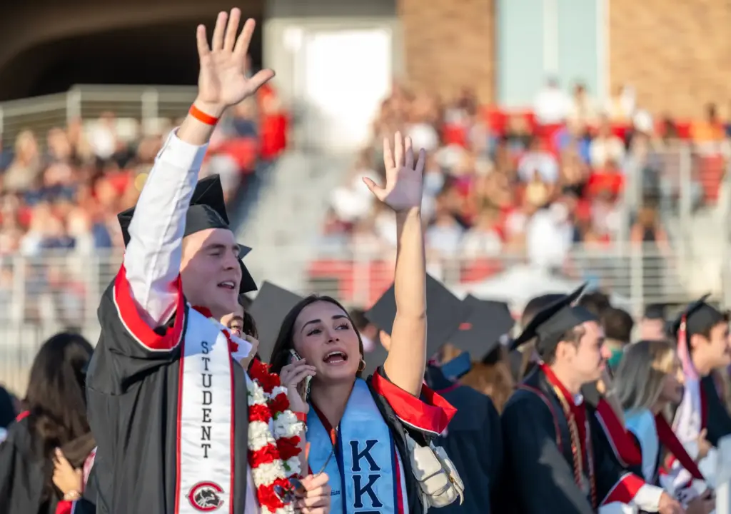 Graduates wave to their loved ones in the stands as...
