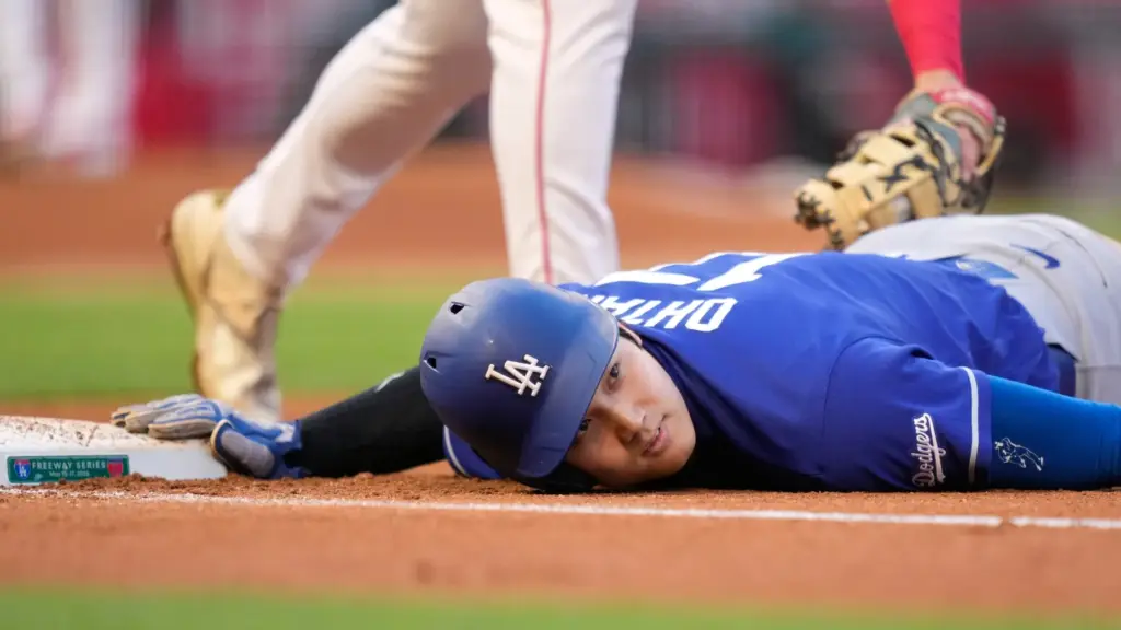 Dodgers’ Shohei Ohtani, below, dives back to first under the...
