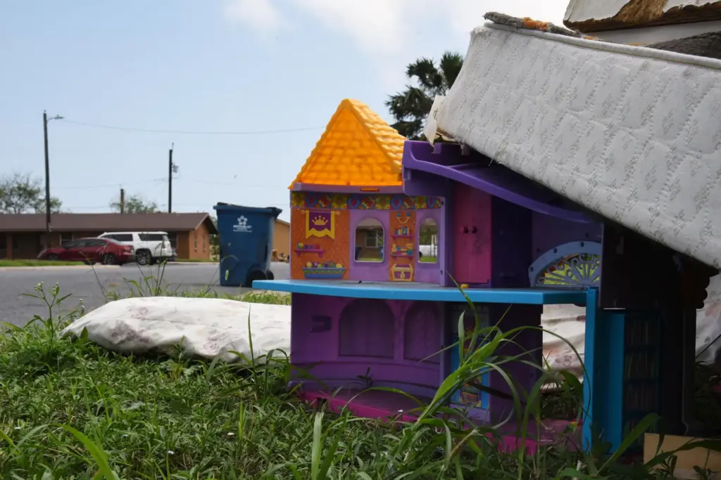 A plastic dollhouse sits among a pile of furniture discarded in a public housing subdivision.