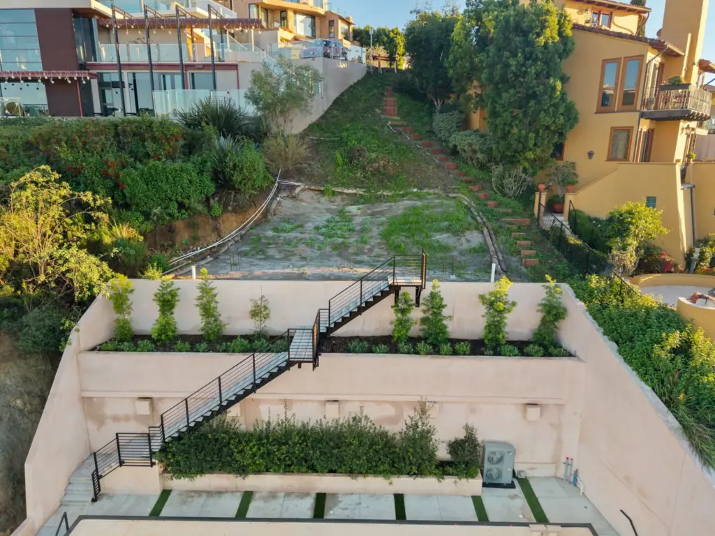 Black metal staircases scale the tiered retaining wall towato the...