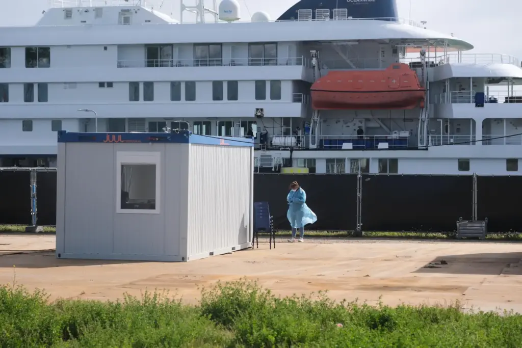 A woman in protective gear stands in front of the MV Hondius cruise ship