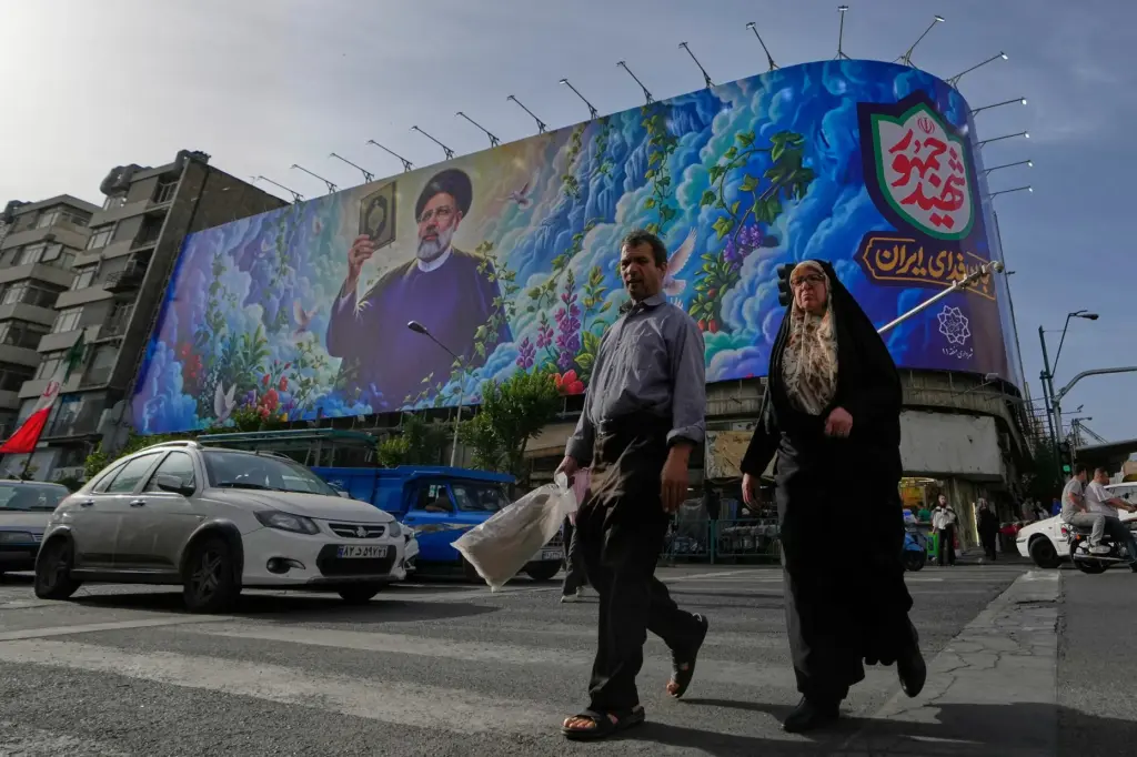 People cross an intersection in front of a billboard of the late Iranian President Ebrahim Raisi.