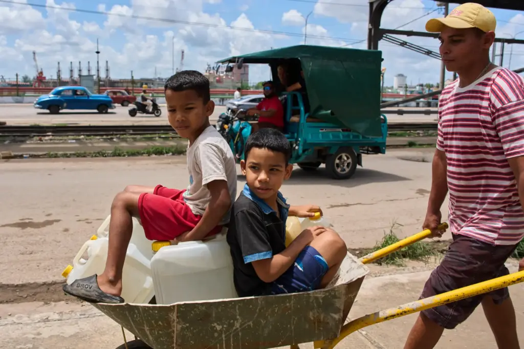 A man transports containers of water with his children in...