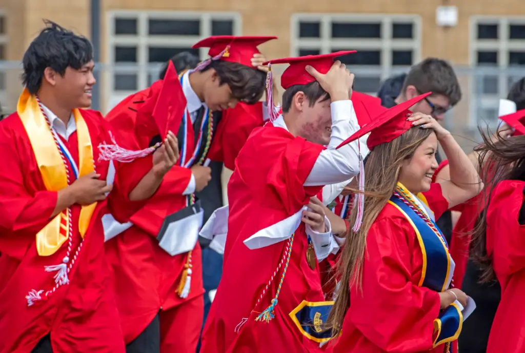 Graduates struggle to keep their hats on during a blustery...