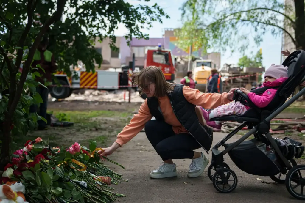 A woman lays flowers in front of a house heavily damaged after a Russian strike.