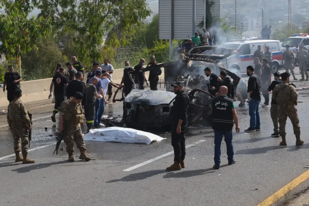 Security forces and emergency responders gather around a charred vehicle...