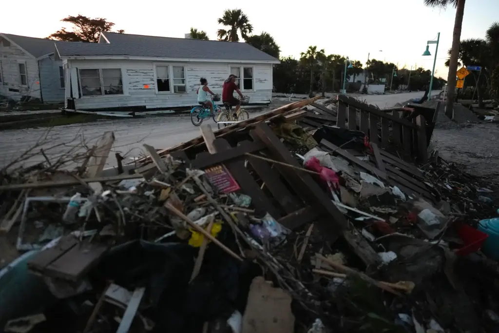 FILE – People bike past damaged homes and debris left...