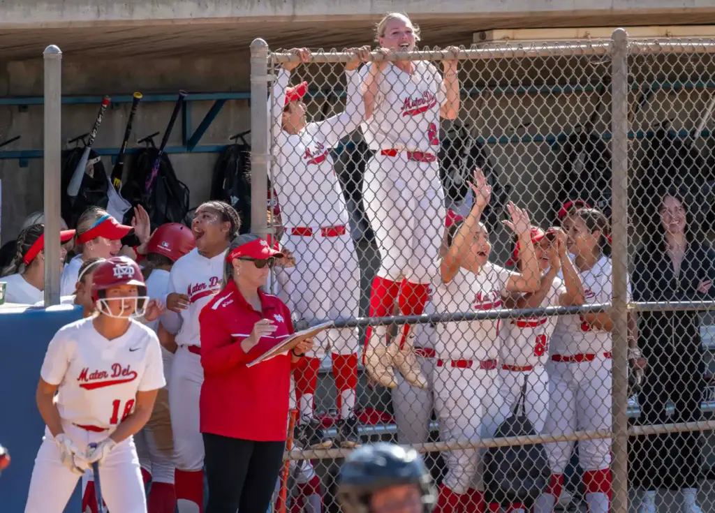 Mater Dei players climb the dugout fence as they cheer...