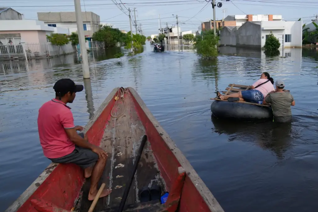 FILE – Residents wade through a flooded neighborhood in Monteria,...