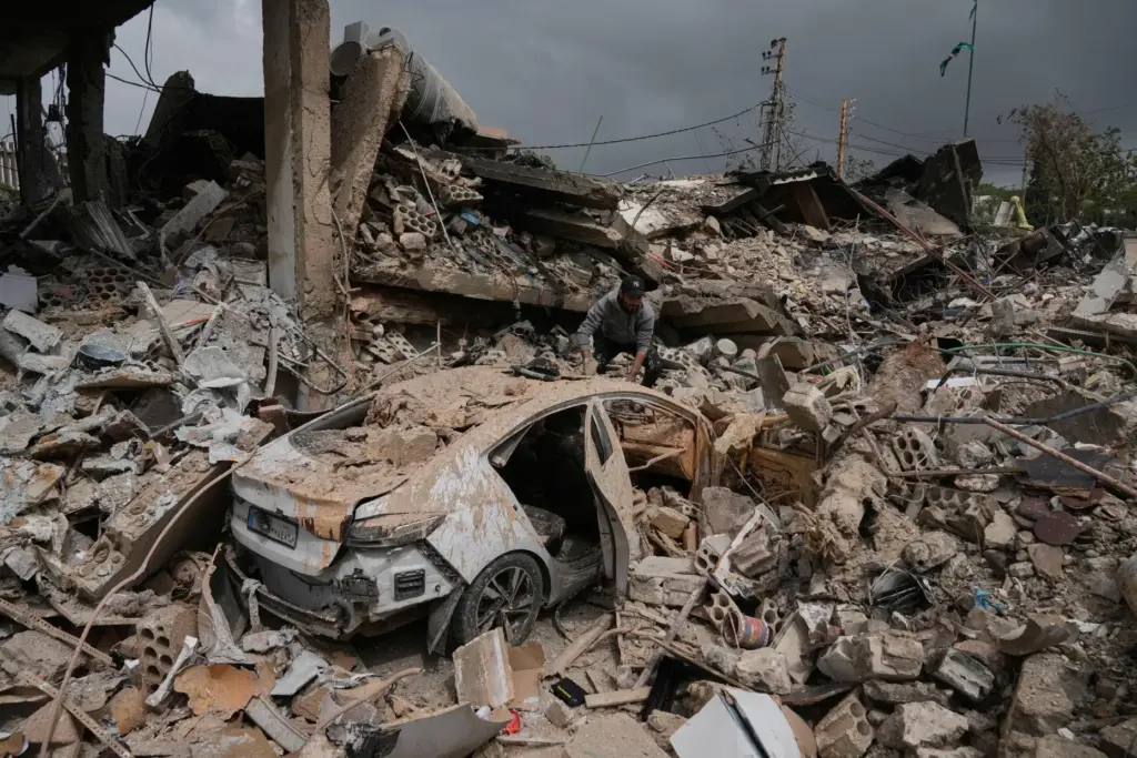 A man inspects his damaged car amid the rubble of shops destroyed in Israeli airstrikes.