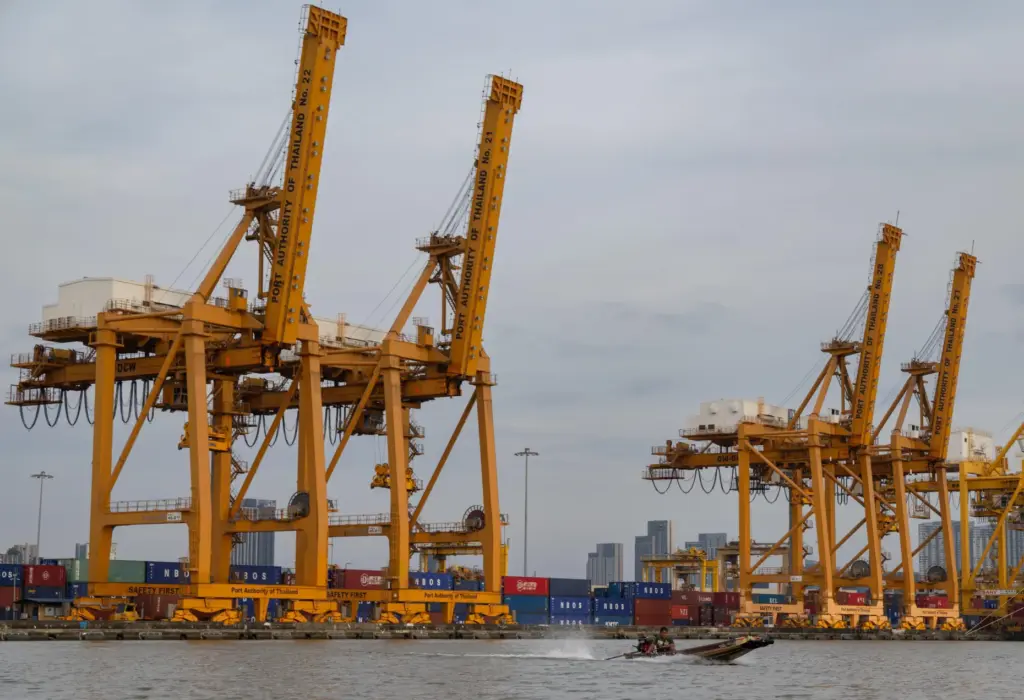 A small boat splashes past a row of ship-to-shore cranes at Khlong Toei Pier.