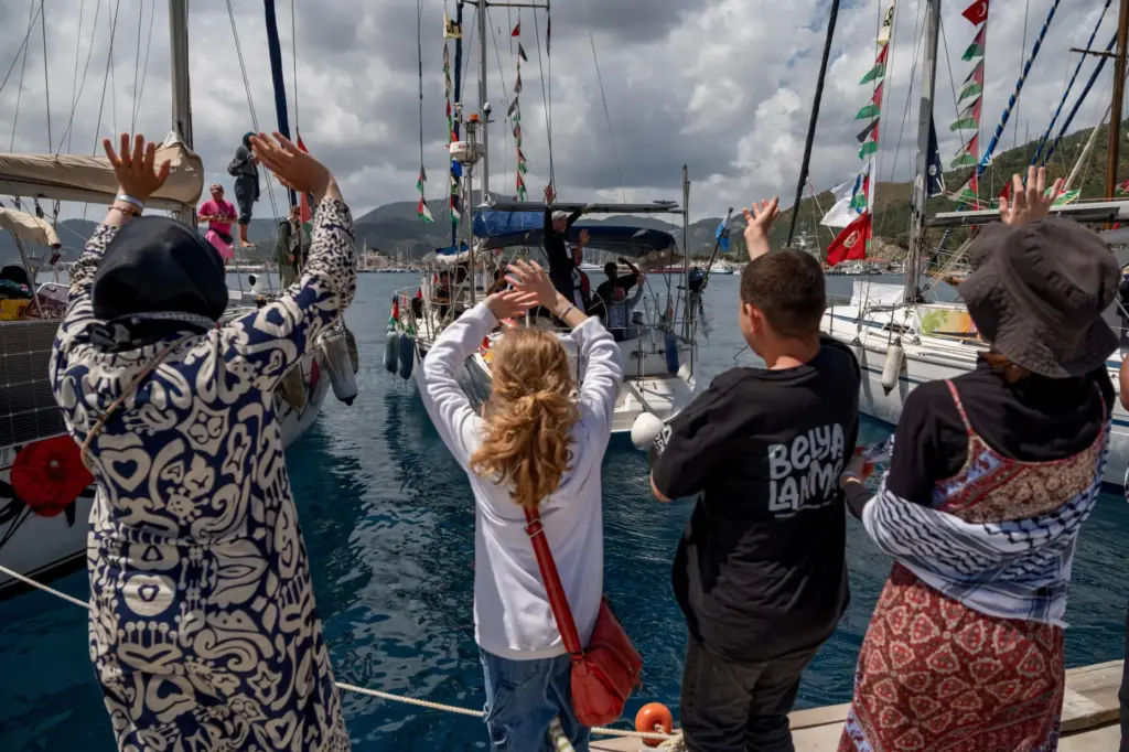 People wave to boats belonging to the Global Sumud Flotilla.