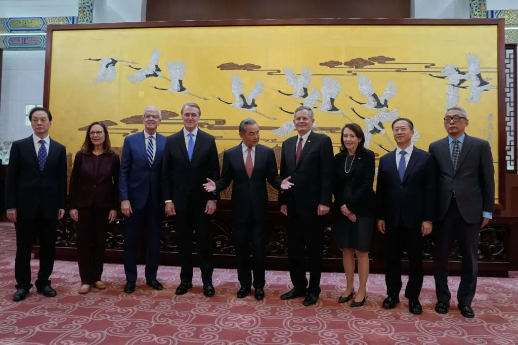 Chinese Foreign Minister Wang Yi gestures next to Steve Daines and David Perdue.