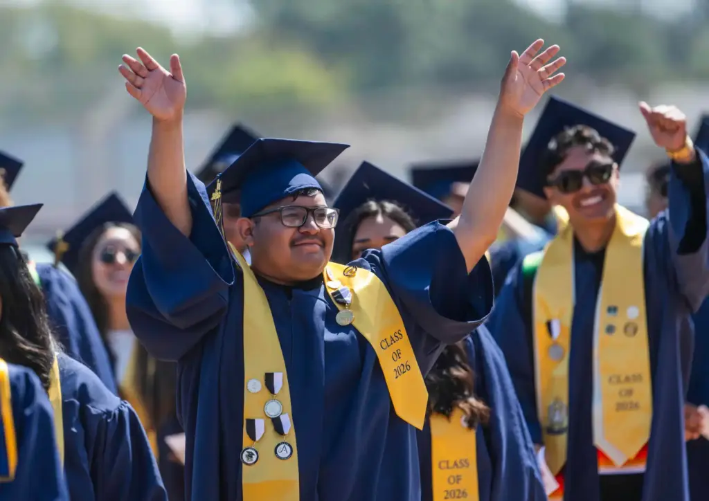 A graduating senior waves to family as he walks into...