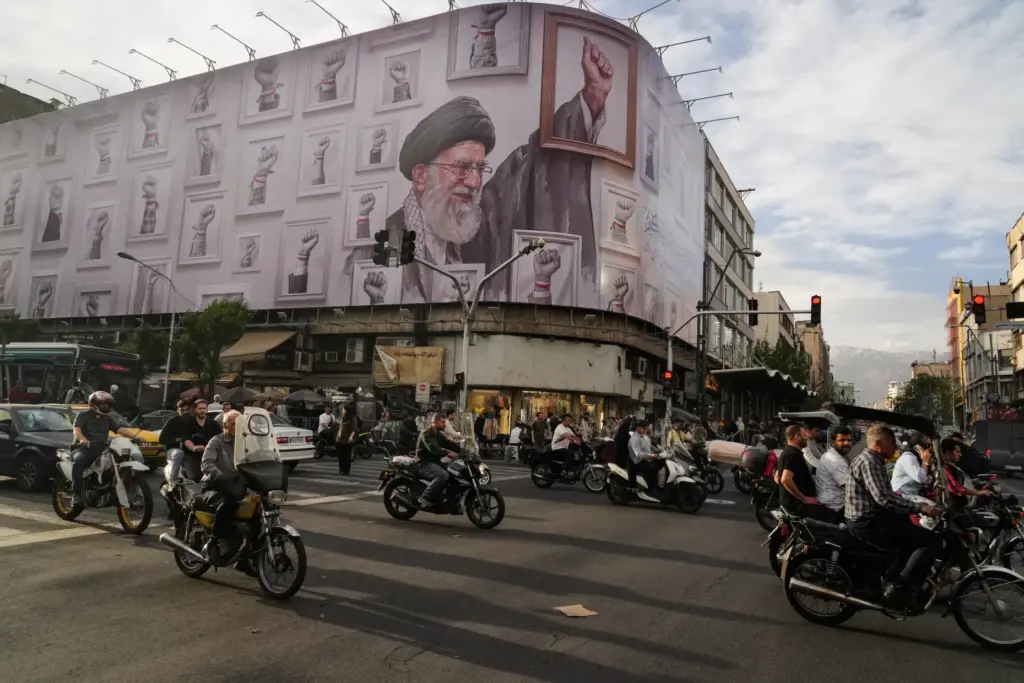 Motorbikes drive past a billboard showing the late Iranian Supreme Leader Ayatollah Ali Khamenei.