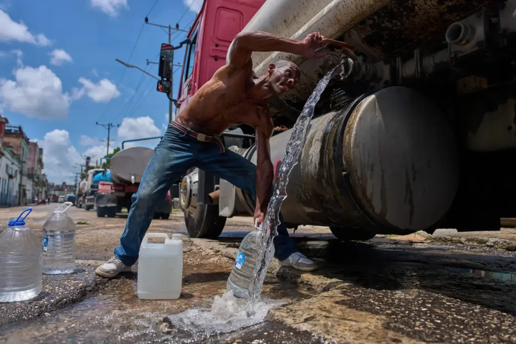 A man fills water jugs from a tanker truck in...