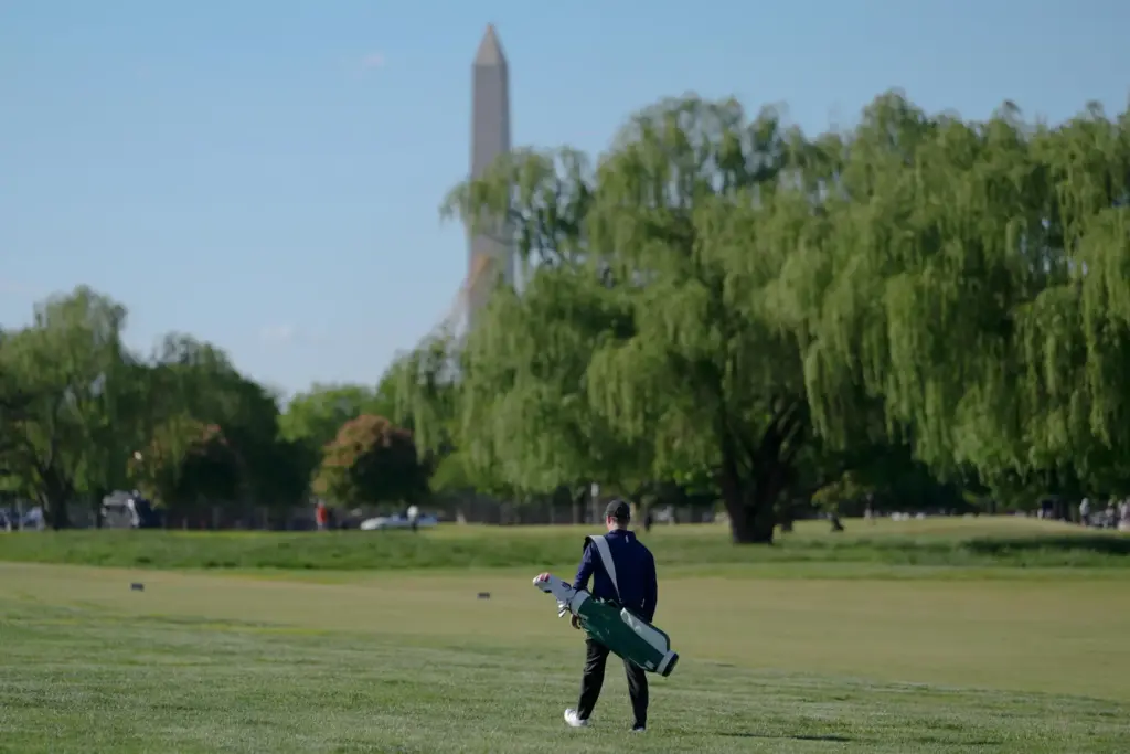 The Washington Monument is seen as a golfer walks the East Potomac Golf Course.