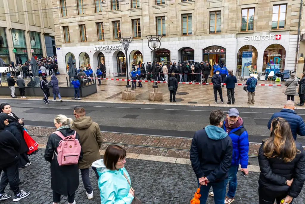 Swiss police officers secure the area where customers queue to...
