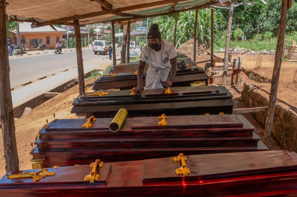 Djakisa Christian, 18, a funeral home manager, dusts coffins for sale