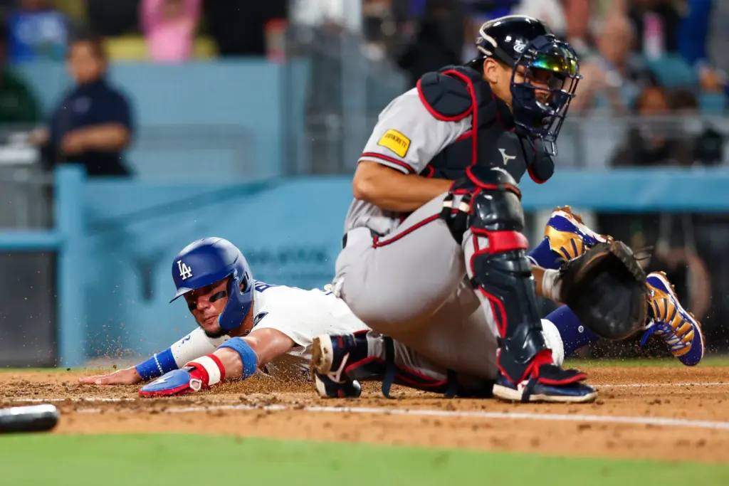 The Dodgers’ Miguel Rojas, left, slides across home plate to...