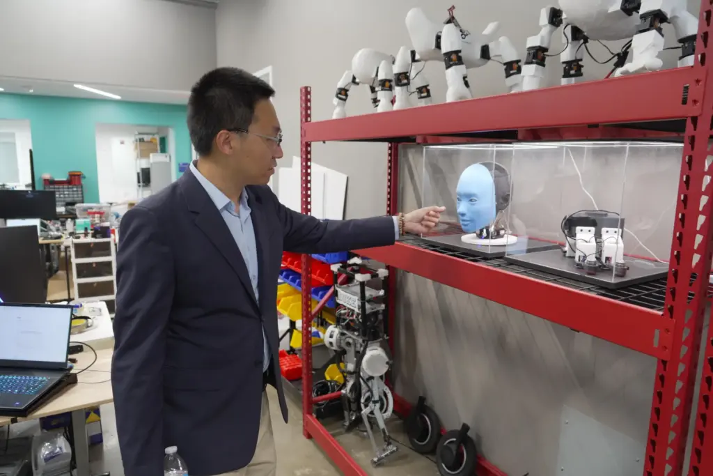 Professor Boyuan Chen gestures toward a humanoid robot at Duke...