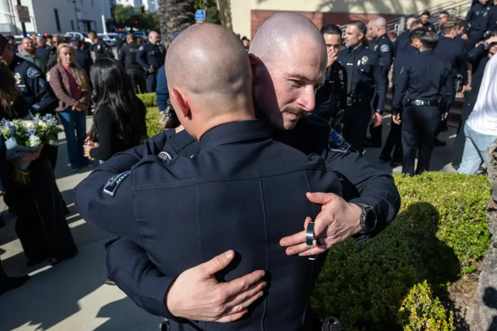 Spike’s handler, Burbank Police Officer Salas hugs a colleague during...
