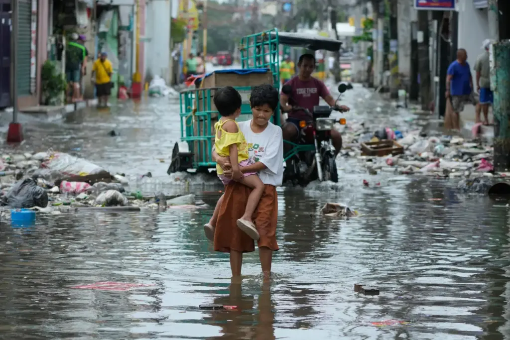 FILE – A woman and child crosses a flooded street...