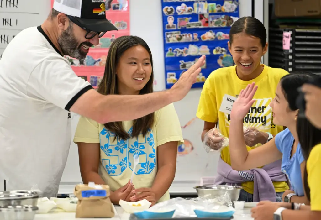 Camp director Erick Fienberg, left, high-fives Mia Shih as she...