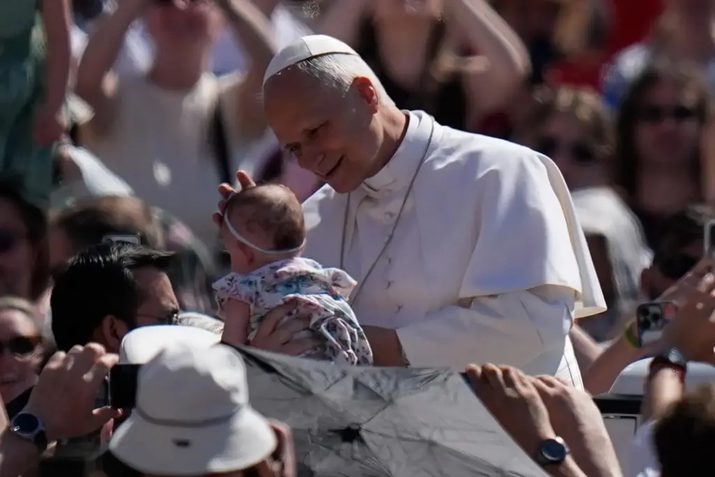 Pope Leo XIV blesses a newborn as he arrives for his weekly general audience.