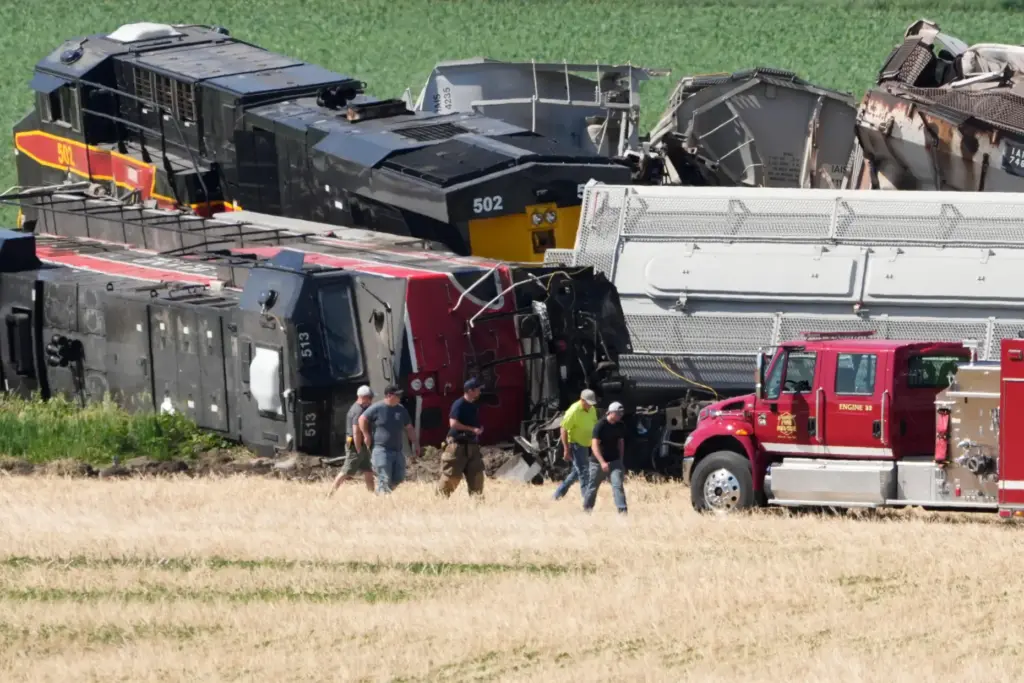 Workers and first responders walk past damage after a train...