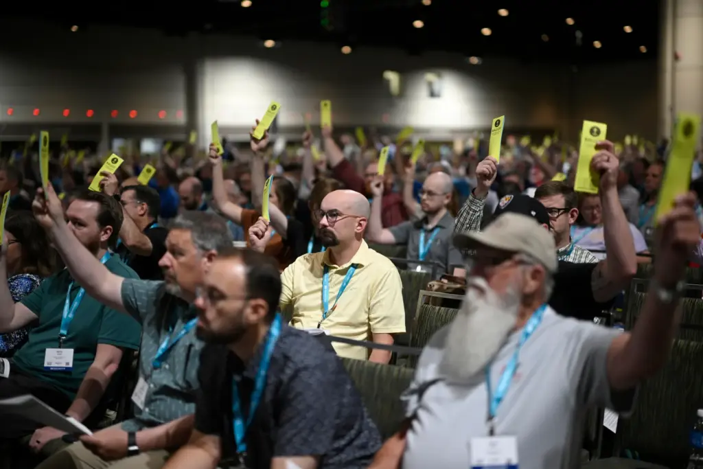 Attendees hold up their ballots while voting on a motion...