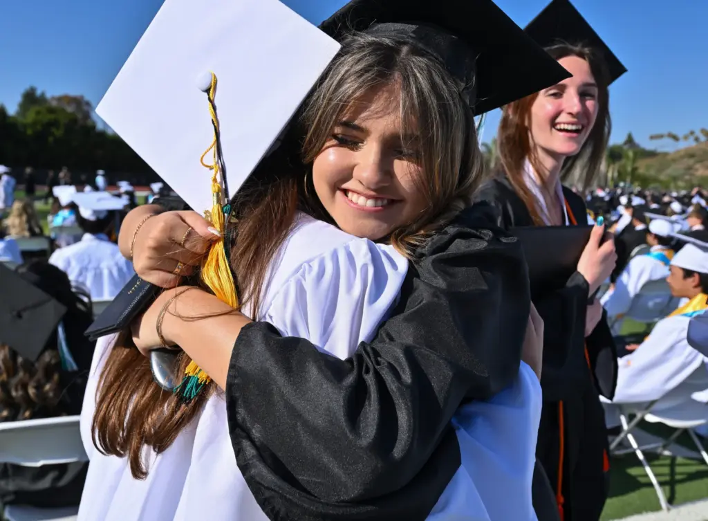 Graduate Hailey McKenney hugs classmate Sophia Machado after getting their...