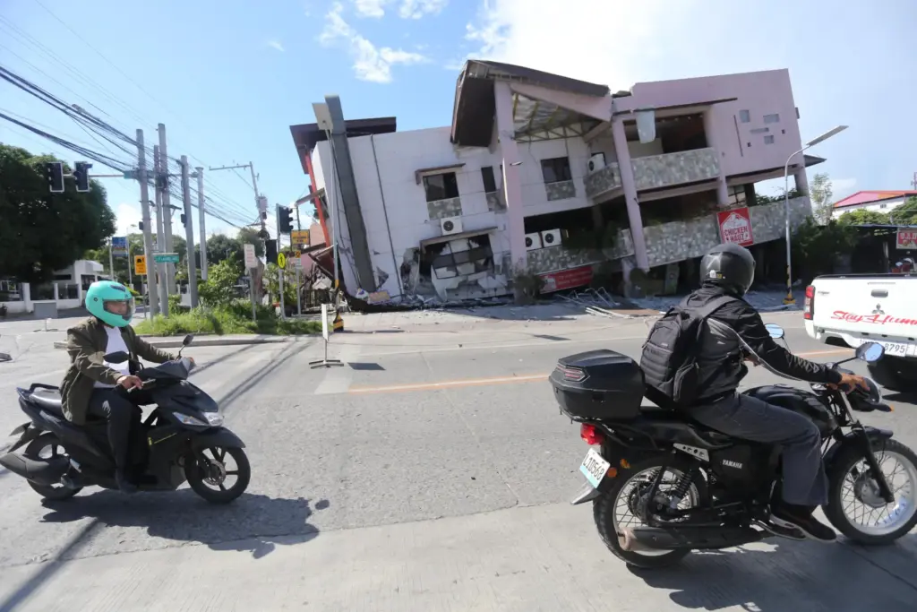People on motorcycles pass by a collapsed structure after an...
