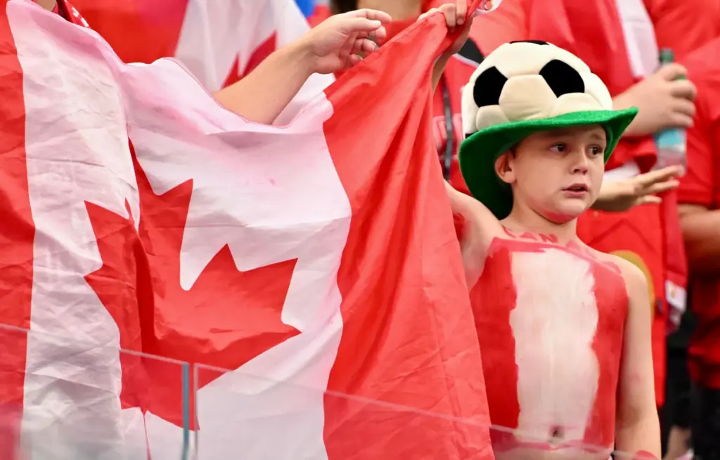 A young Canadian fan wearing a soccer hat and holding...